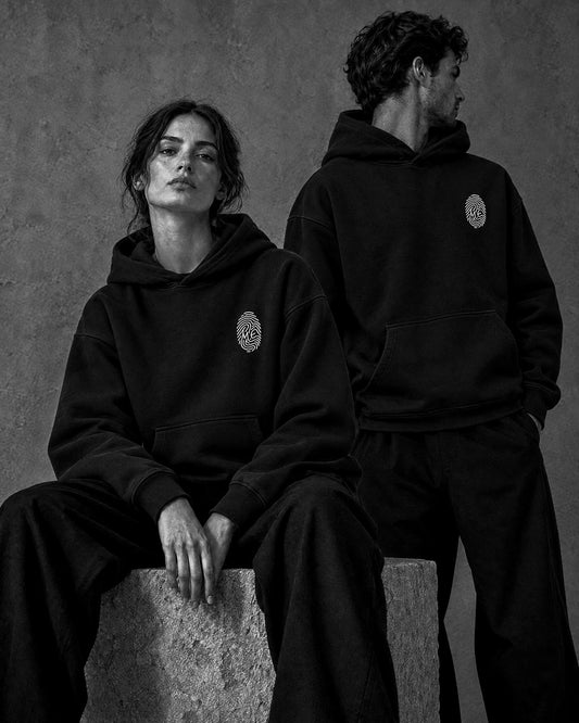 Le Hoodie Signature noir porté en duo — femme assise et homme debout