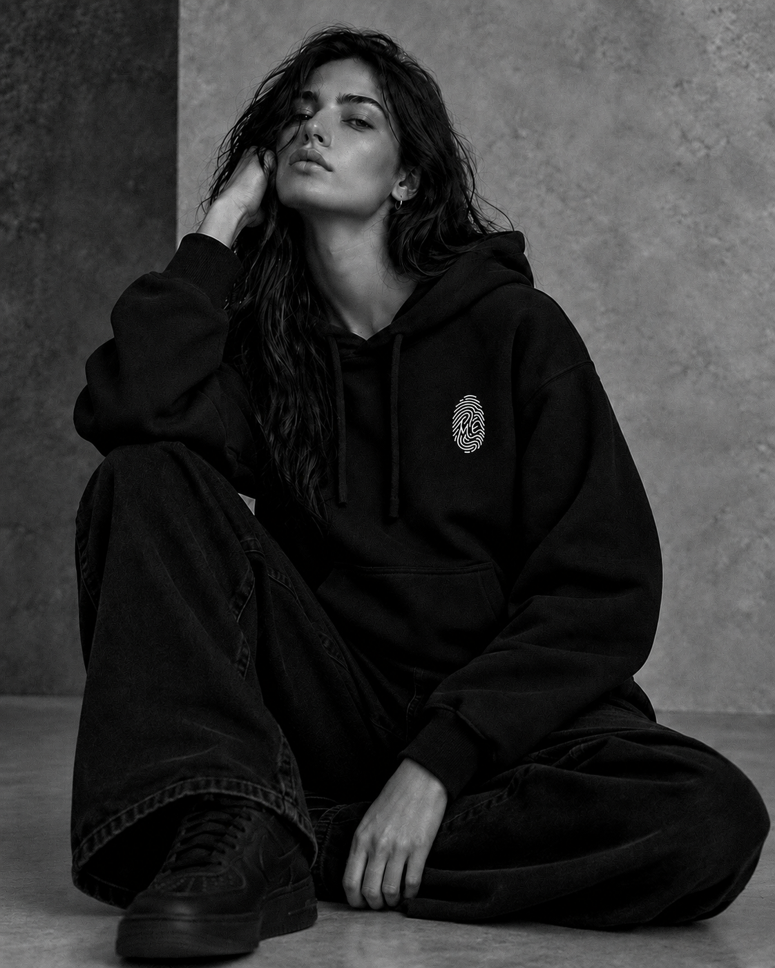 Le Hoodie Signature noir porté par une femme assise — empreinte M.E brodée sur la poitrine