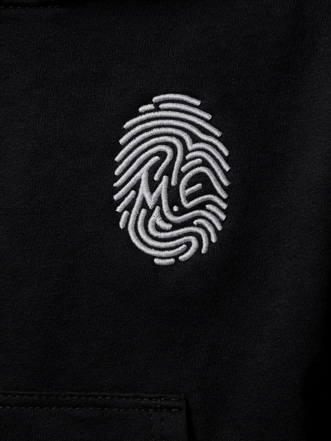 Détail de l’empreinte M.E blanche brodée — Hoodie Signature noir