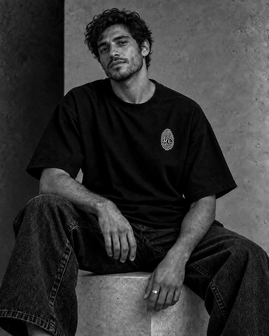 L’Empreinte — t-shirt oversize noir porté par un homme assis, vue de face